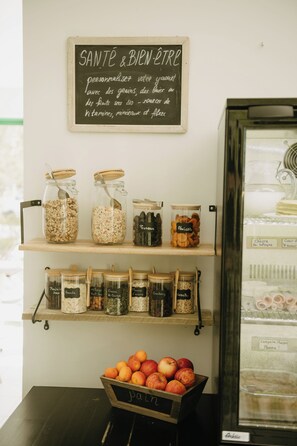 A shelf with jars of grains and nuts, a chalkboard sign, and a bowl of fruits. - Hôtel du Chateau (Tour-en-Sologne)