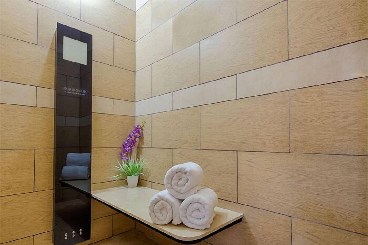 A modern bathroom with a wooden floor, a glass shower enclosure, a small potted plant, and neatly rolled towels on a shelf.