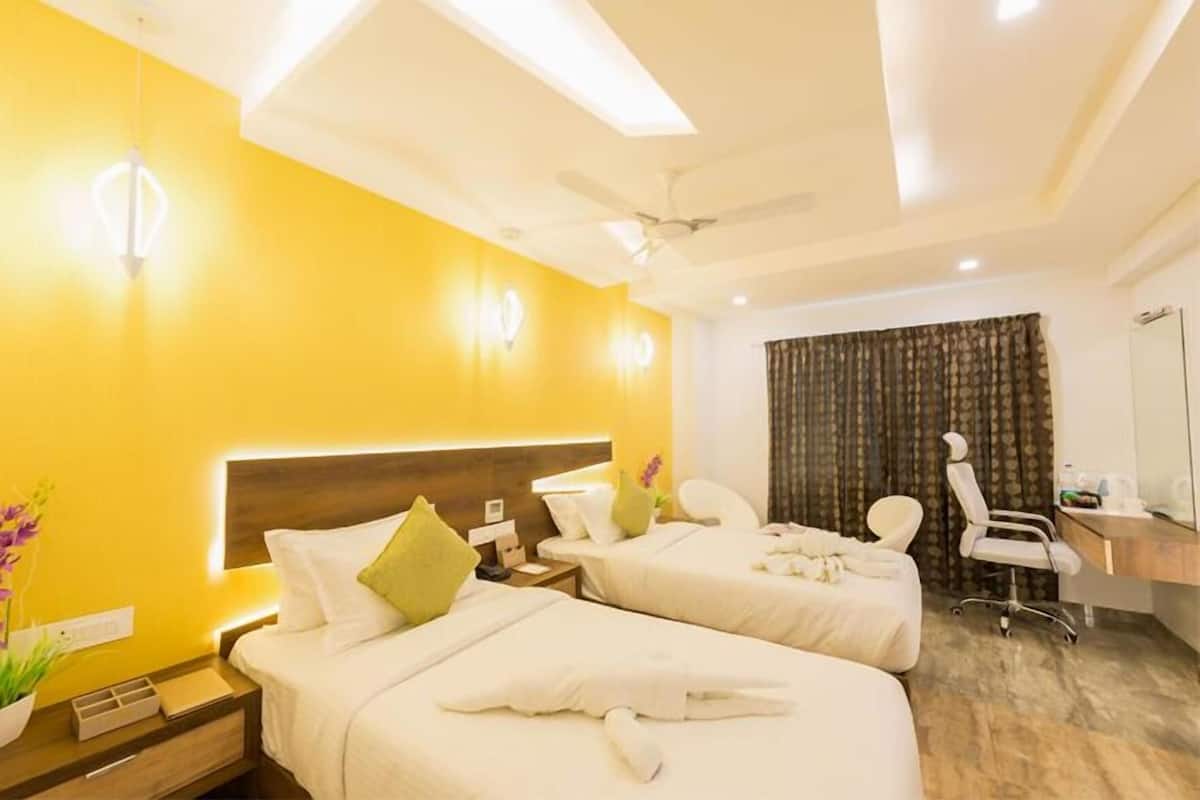 A hotel room with two beds, a desk, a chair, a ceiling fan, and a large window with curtains.