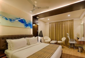 Habitación de hotel con una cama grande, ventilador de techo, escritorio con silla, espejo y ventana con cortinas.