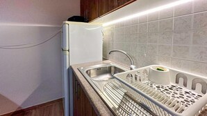 Keittiössä on valkoinen jääkaappi, ruostumattomasta teräksestä valmistettu pesuallas ja astiateline.