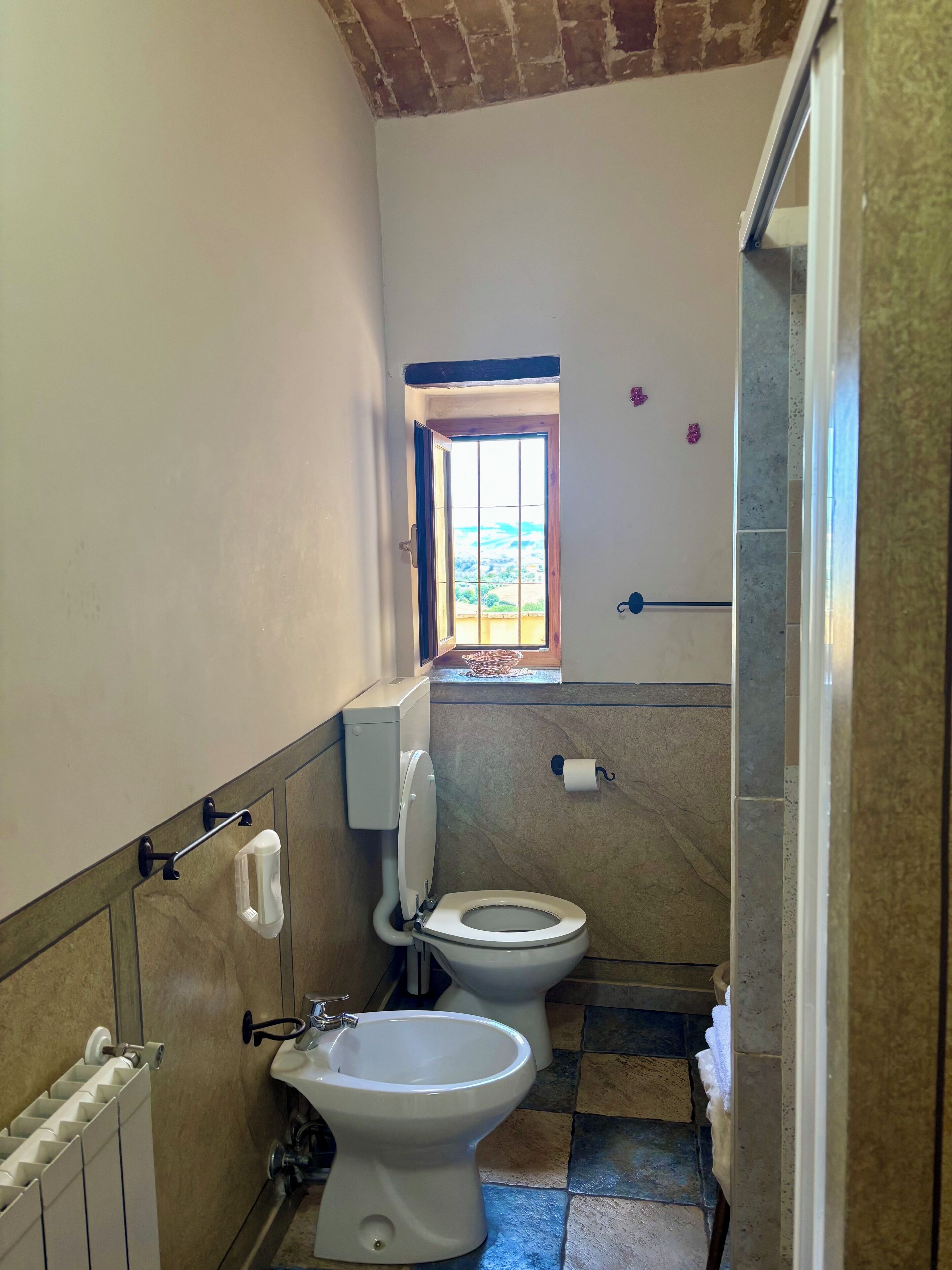 A small bathroom with a toilet, bidet, and a window.