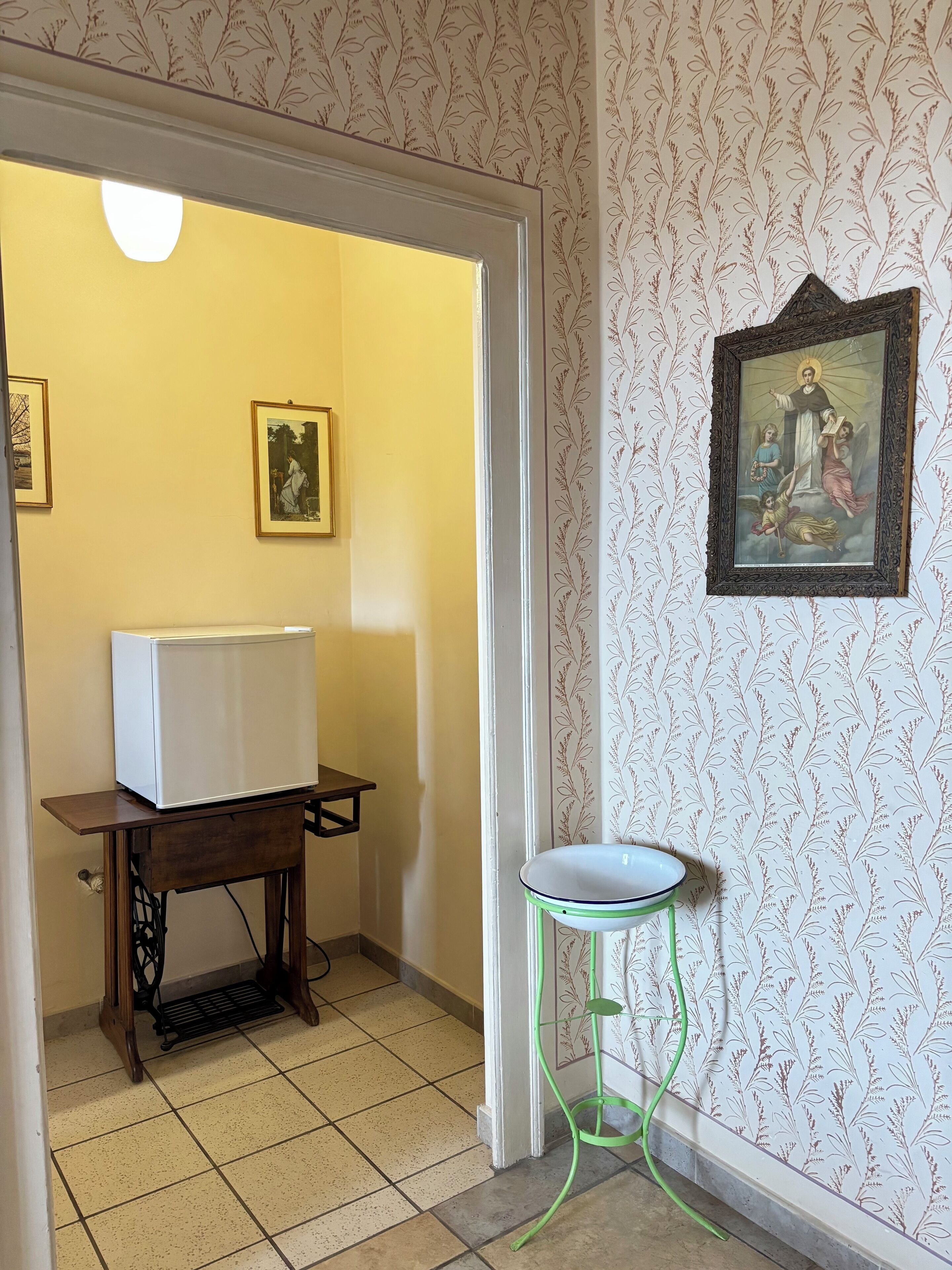 A room with a sewing machine, a white refrigerator, and a green stool.