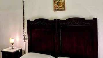 Quarto com cabeceira de madeira, cama com roupa de cama branca, mesa de cabeceira com abajur e um objeto decorativo na parede.