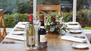A dining table set with wine bottles, glasses, and a floral centerpiece. - The Grange House Self Catering (Keswick)