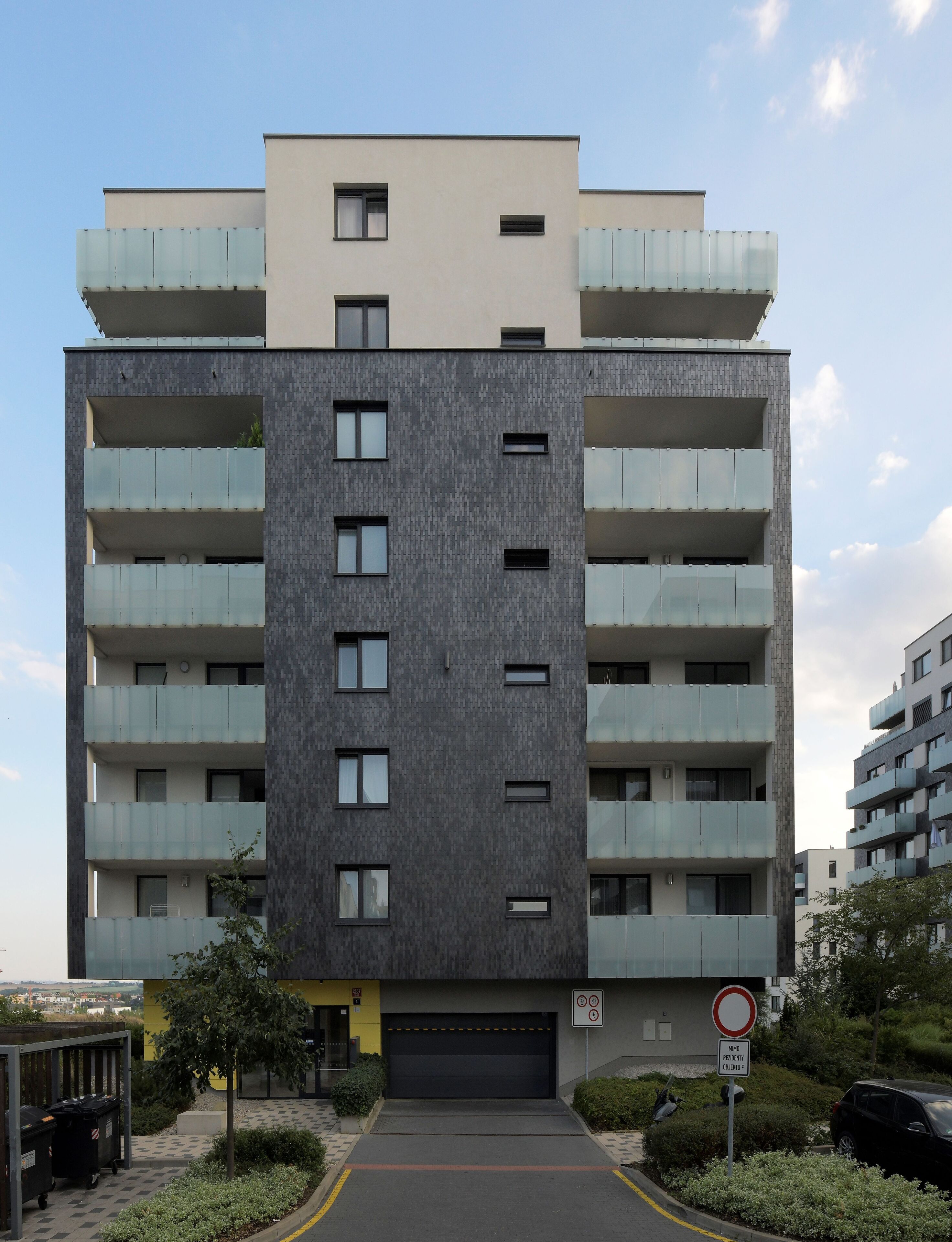 A multi-story residential building with balconies, a garage, and a parking area.