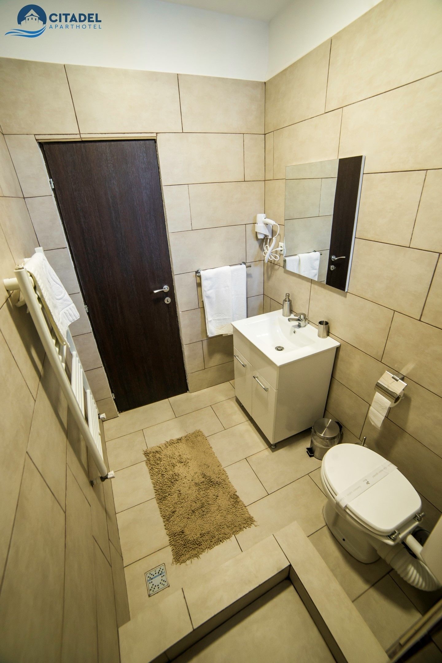 A modern bathroom with a dark wooden door, white sink, and toilet.