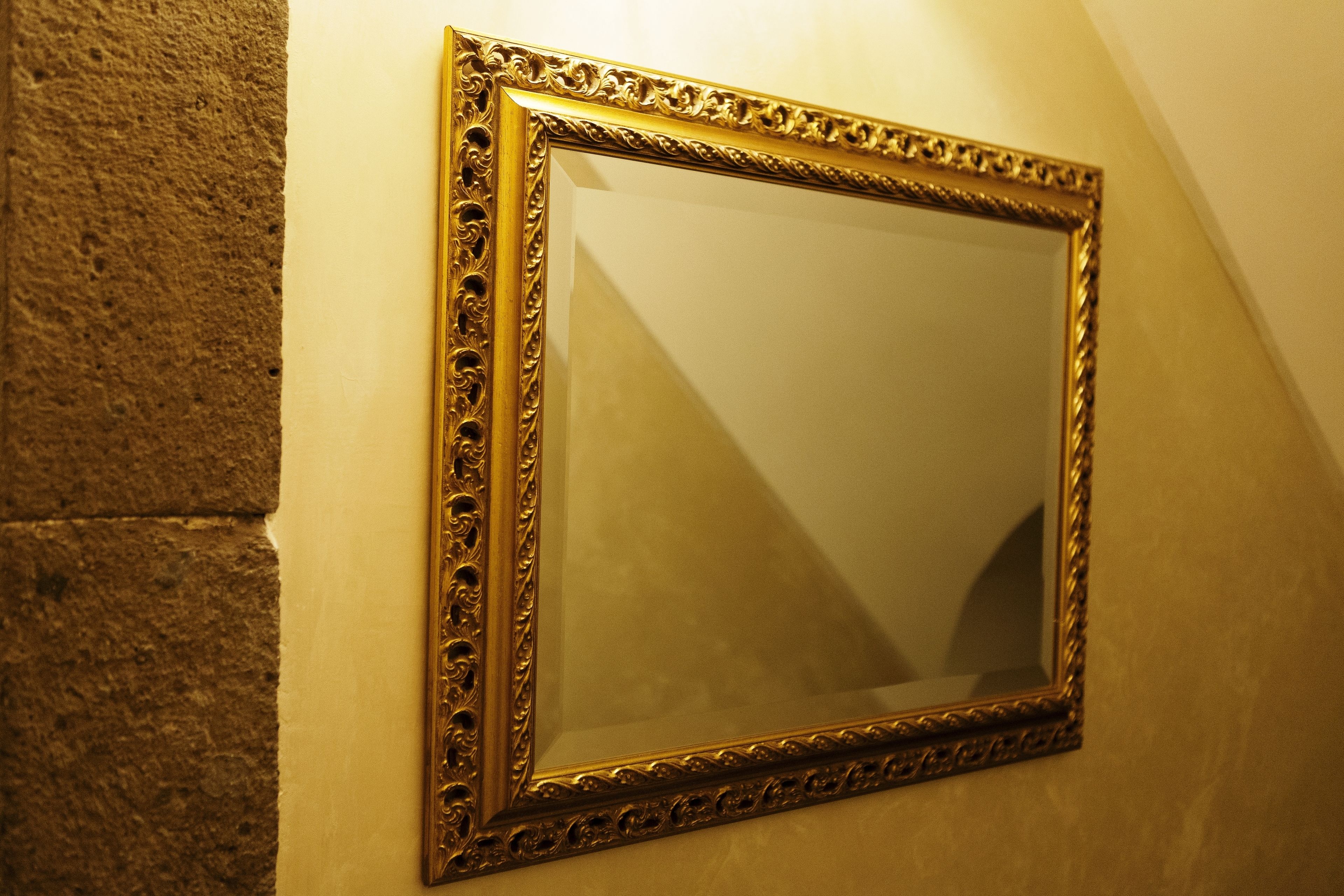 A mirror with an ornate gold frame mounted on a textured wall.