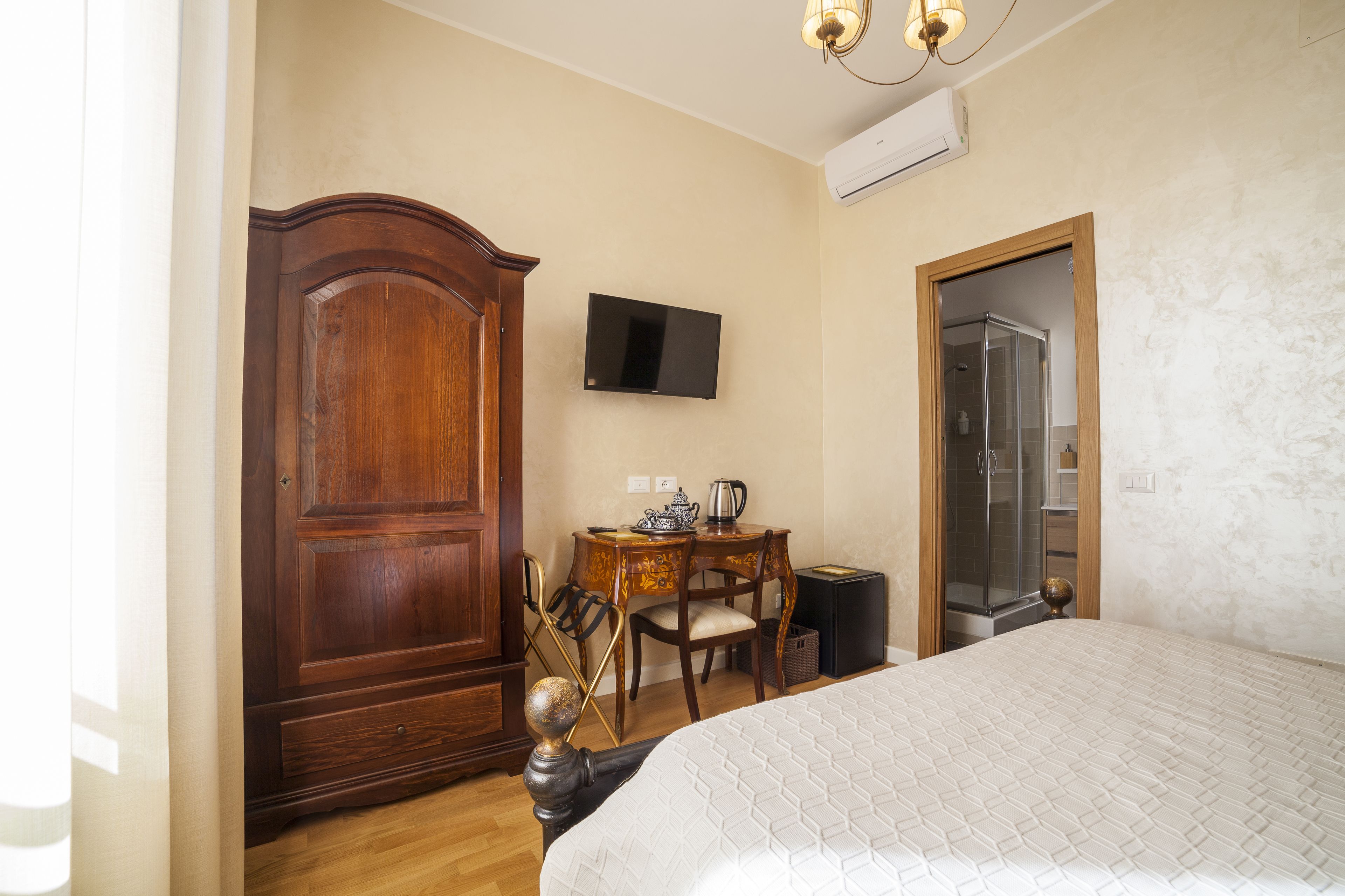 Une chambre avec un grand lit, une armoire en bois, un bureau avec une chaise, une télévision et un espace douche.