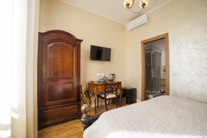 A bedroom with a large bed, a wooden wardrobe, a desk with a chair, a television, and a shower area.