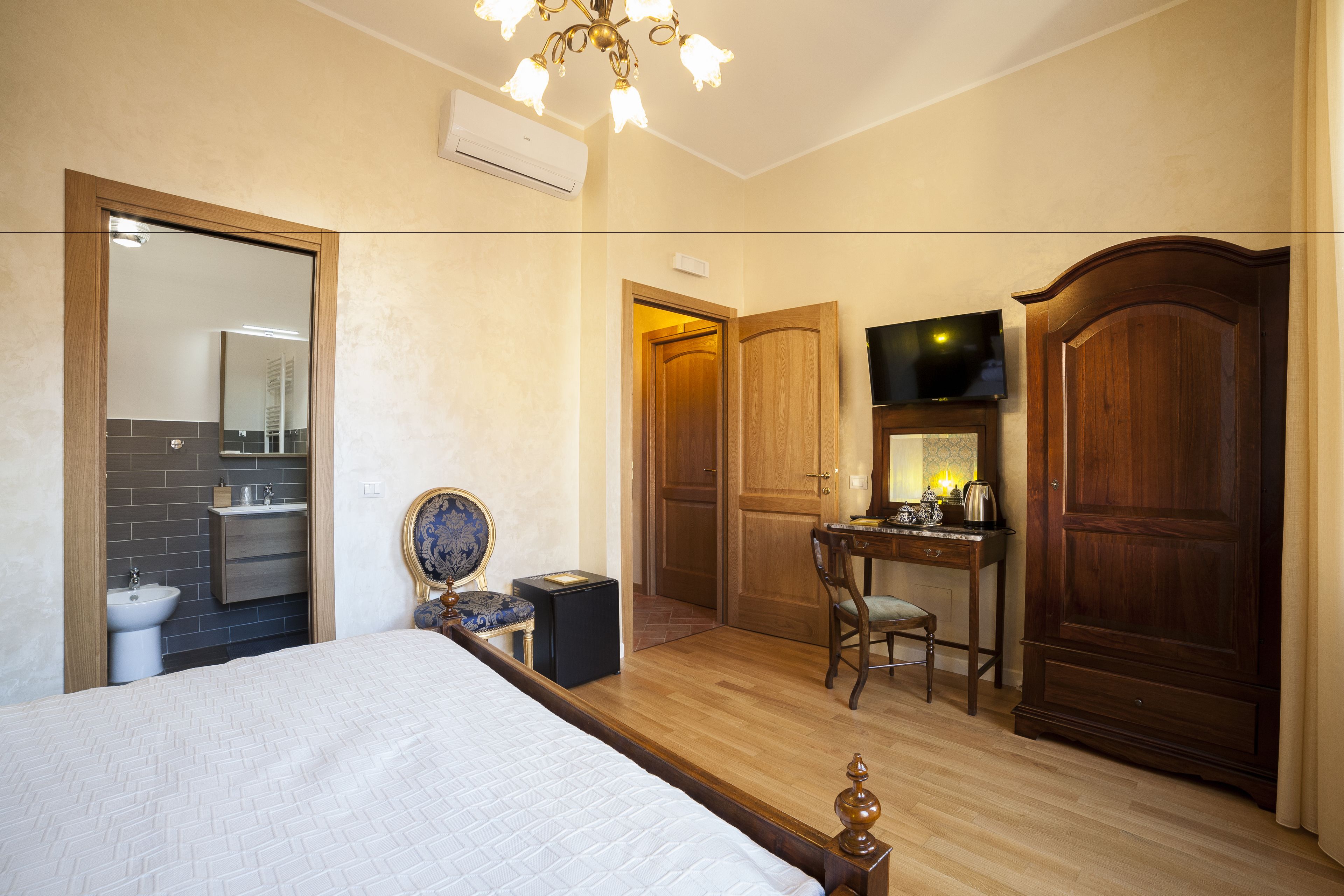 A hotel room with a bed, a desk, a chair, a wardrobe, and a bathroom with a sink and mirror.