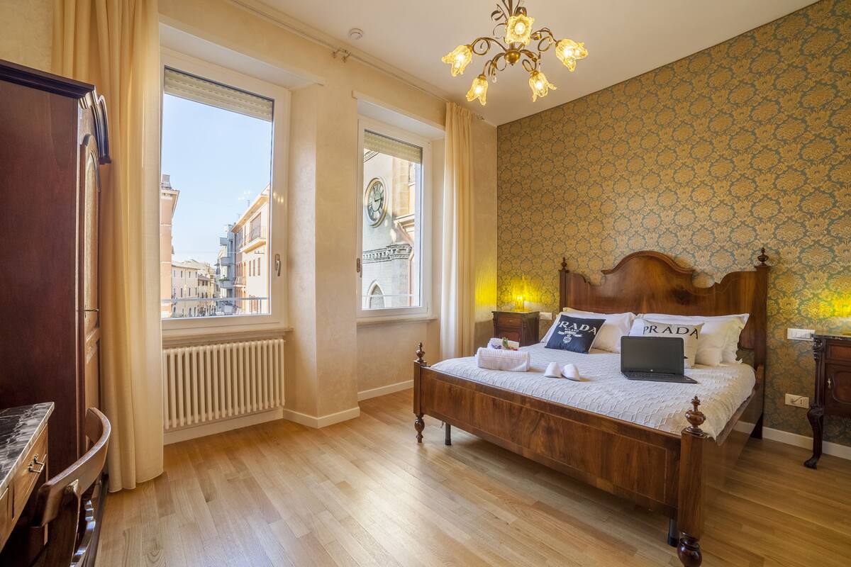 A bedroom with a wooden bed, a view of the city through a window, and a chandelier.