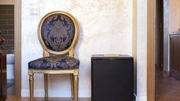 A room with a blue upholstered chair with gold trim, a black cabinet, and a marble wall.