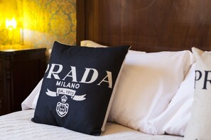 A bed with pillows, one of which has "PRADA MILANO" printed on it.