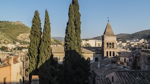 Un pueblo histórico con una iglesia destacada que tiene un campanario, rodeado de edificios tradicionales y altos cipreses.