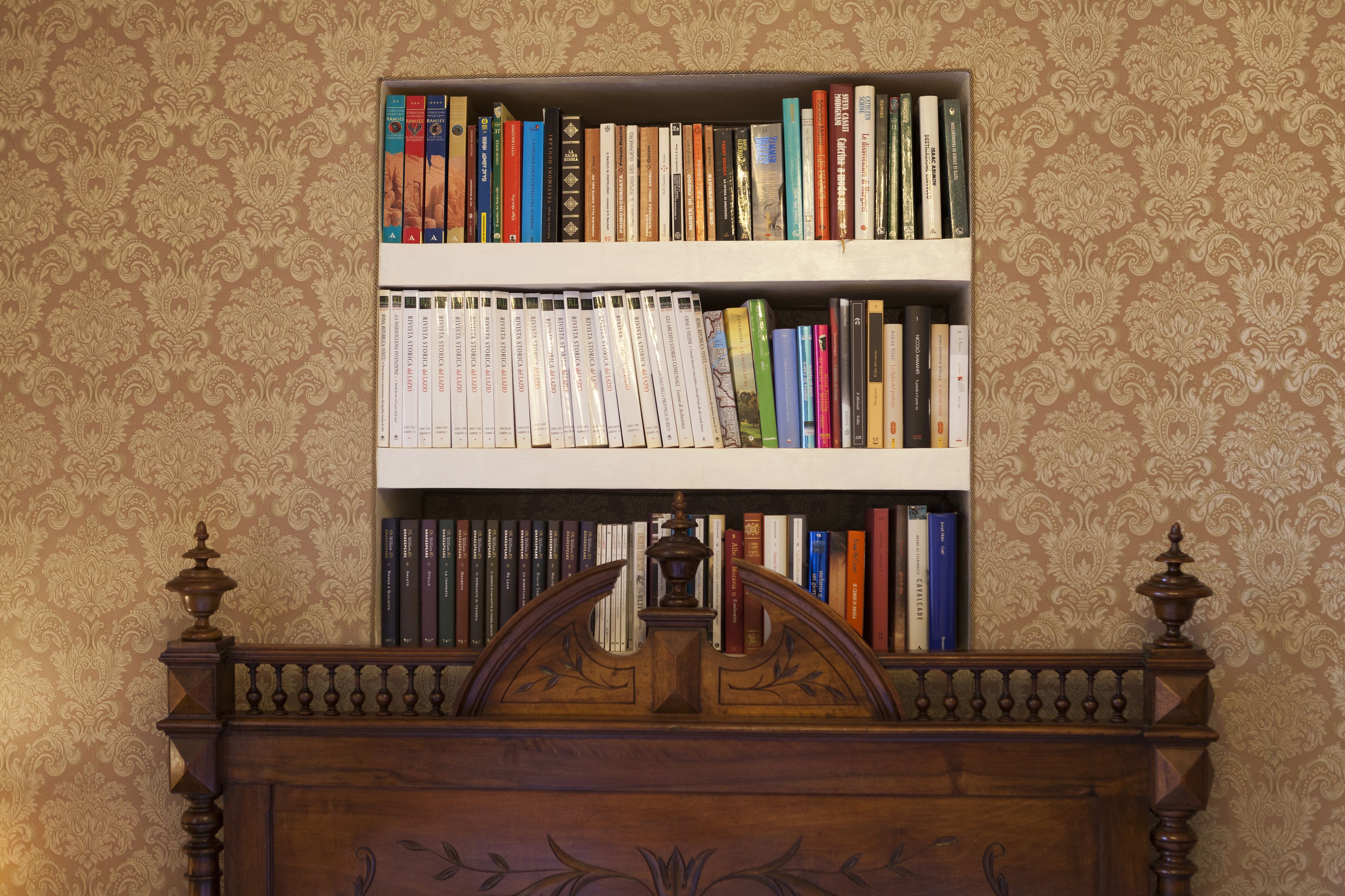 A bookshelf filled with books against a patterned wallpaper background.