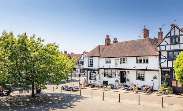 A traditional pub with a white facade and black timber framing, outdoor seating, and a tree in the foreground.