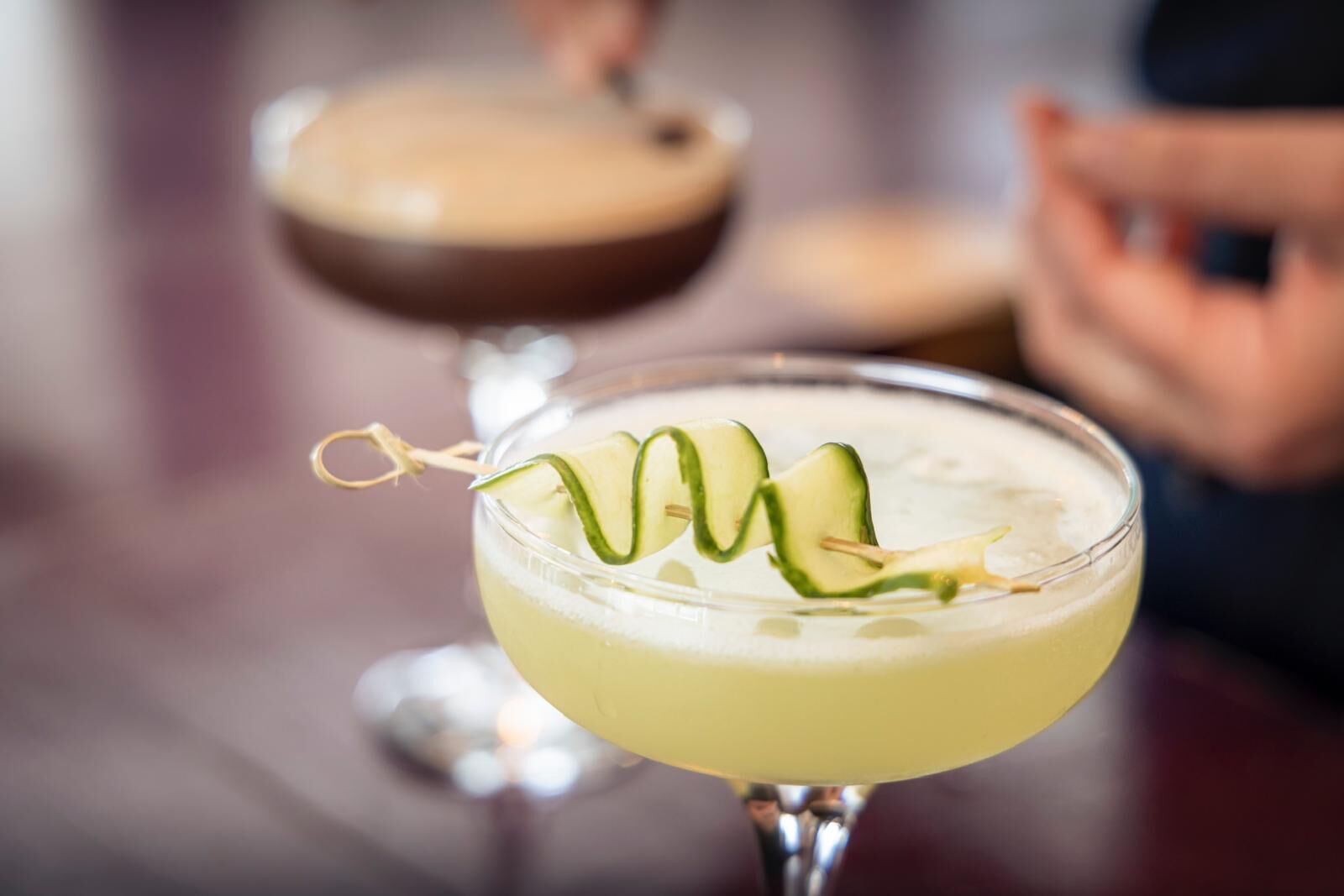A cocktail with cucumber garnish in a glass.