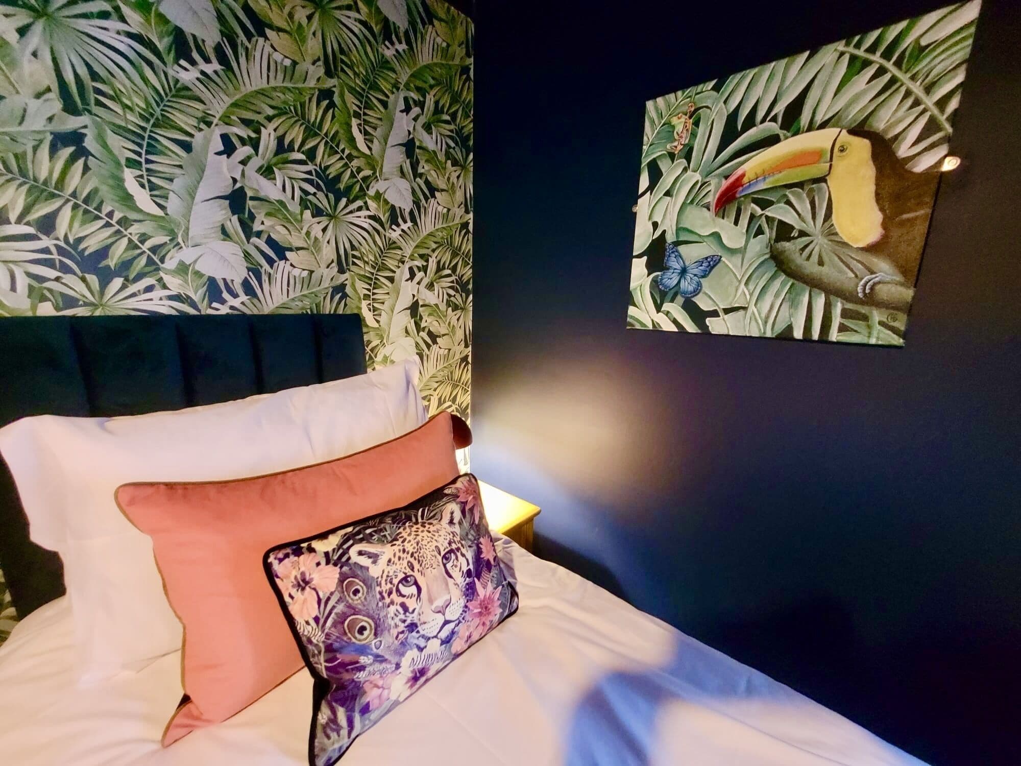 A bed with white and orange pillows, a leopard print pillow, and a tropical leaf wall mural.