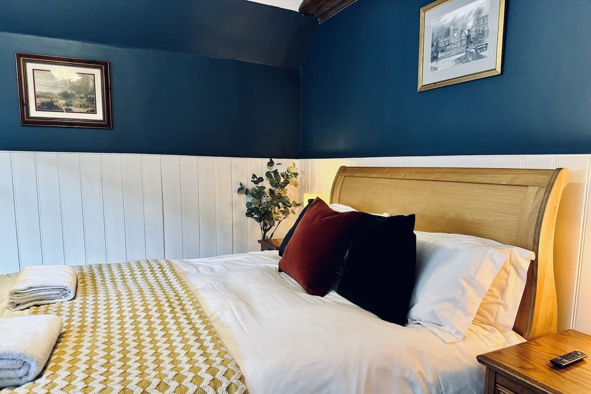 A neatly made bed with a patterned blanket, a bedside table with a remote control, and two framed pictures on the wall.