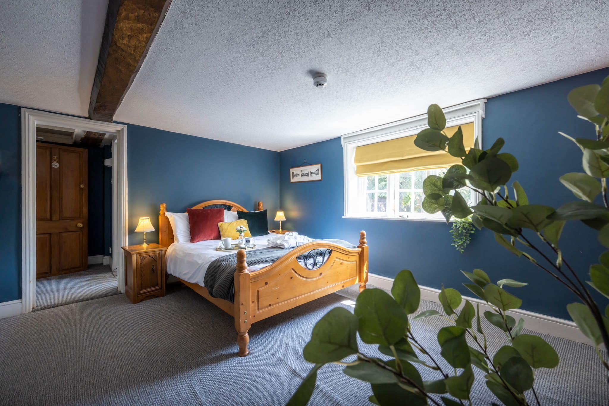 A bedroom with a wooden bed, two bedside tables with lamps, a window with a yellow blind, and a door.