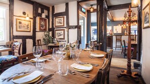 A dining area with a wooden table set for a meal, framed pictures on the walls, and a chandelier.