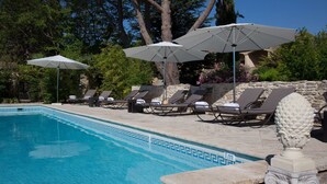 A pool area with lounge chairs and umbrellas, surrounded by stone walls and greenery.