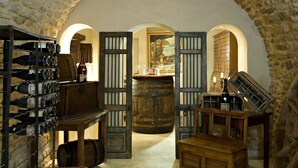 A wine cellar with wooden racks, barrels, and a rustic stone wall.