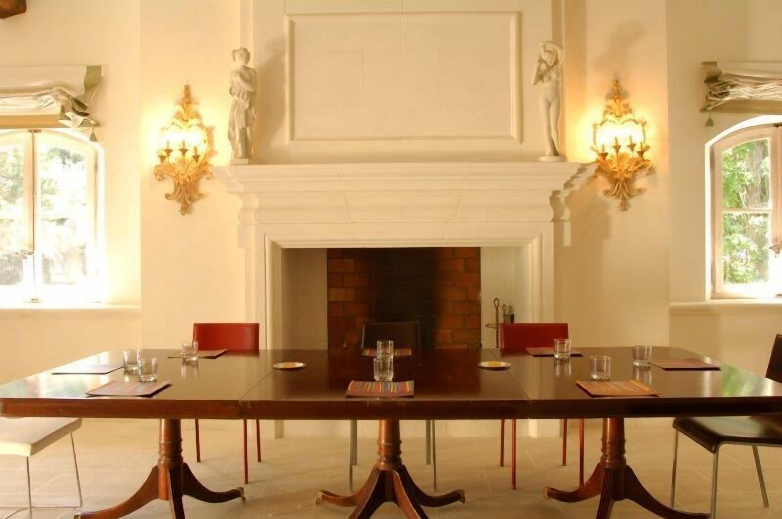 A formal dining room with a long table, chairs, a fireplace, and wall sconces.