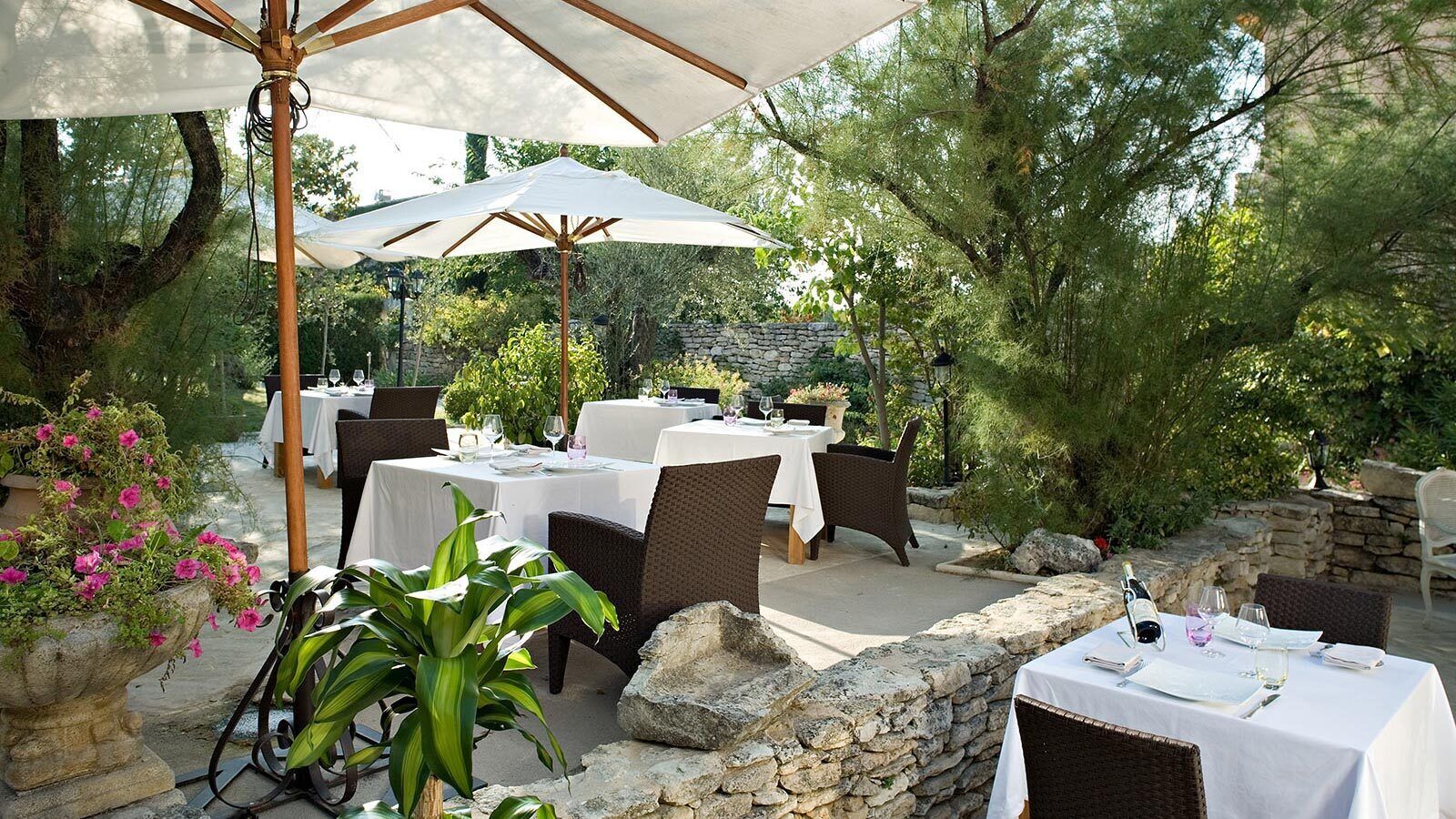 Un espace de restauration en plein air avec des murs en pierre, des meubles en osier et des nappes blanches.