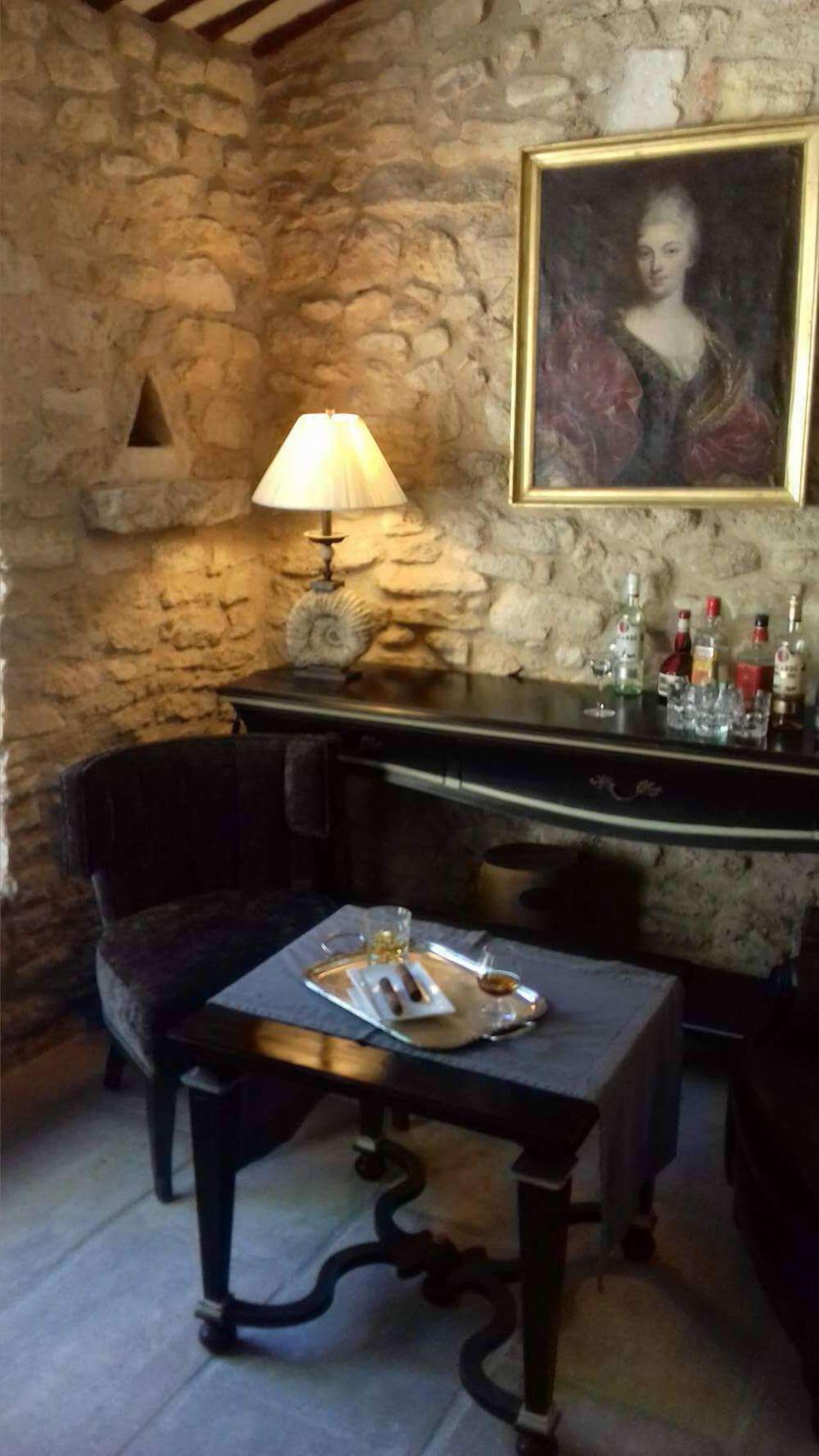 Una habitación de paredes de piedra con una mesa, sillas, una lámpara y un cuadro.