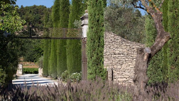 A stone building with a metal gate, surrounded by tall trees and a clear sky.