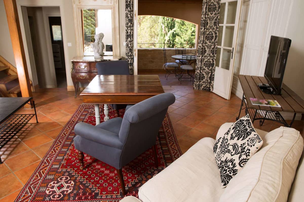 Uma sala de estar com um sofá, uma mesa de jantar e uma cadeira. Há um tapete estampado no chão.