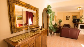 A living room with a wooden cabinet, a large mirror, a red sofa, and a television. - Albergo della Corte (Pescasseroli)