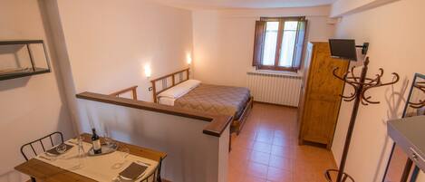 Una habitación compacta con cama, una mesa y sillas, un perchero y un ventanal con cortinas.