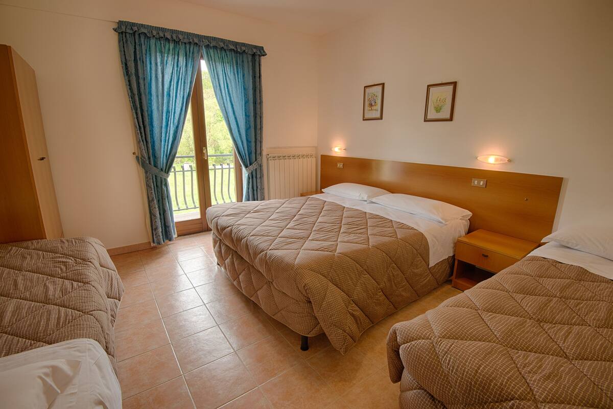 A hotel room with two beds, a wooden headboard, a window with curtains, and two wall-mounted lights.