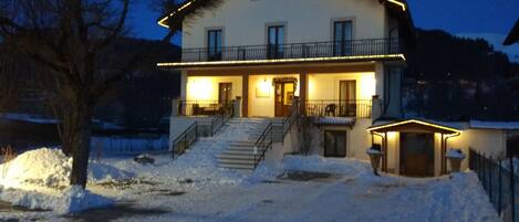 Una casa de dos pisos con un balcón y una escalera que lleva a la entrada, sobre un terreno cubierto de nieve.