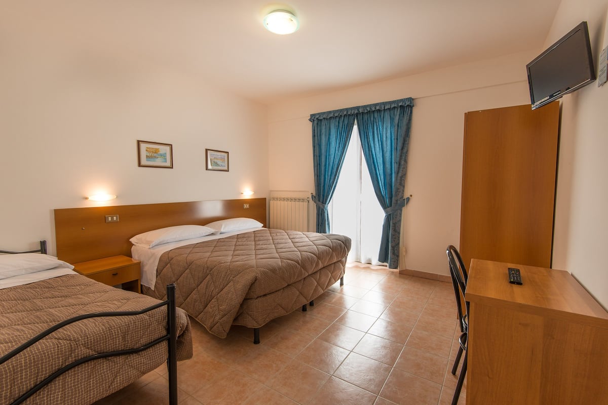A hotel room with two beds, a desk, and a TV on the wall.