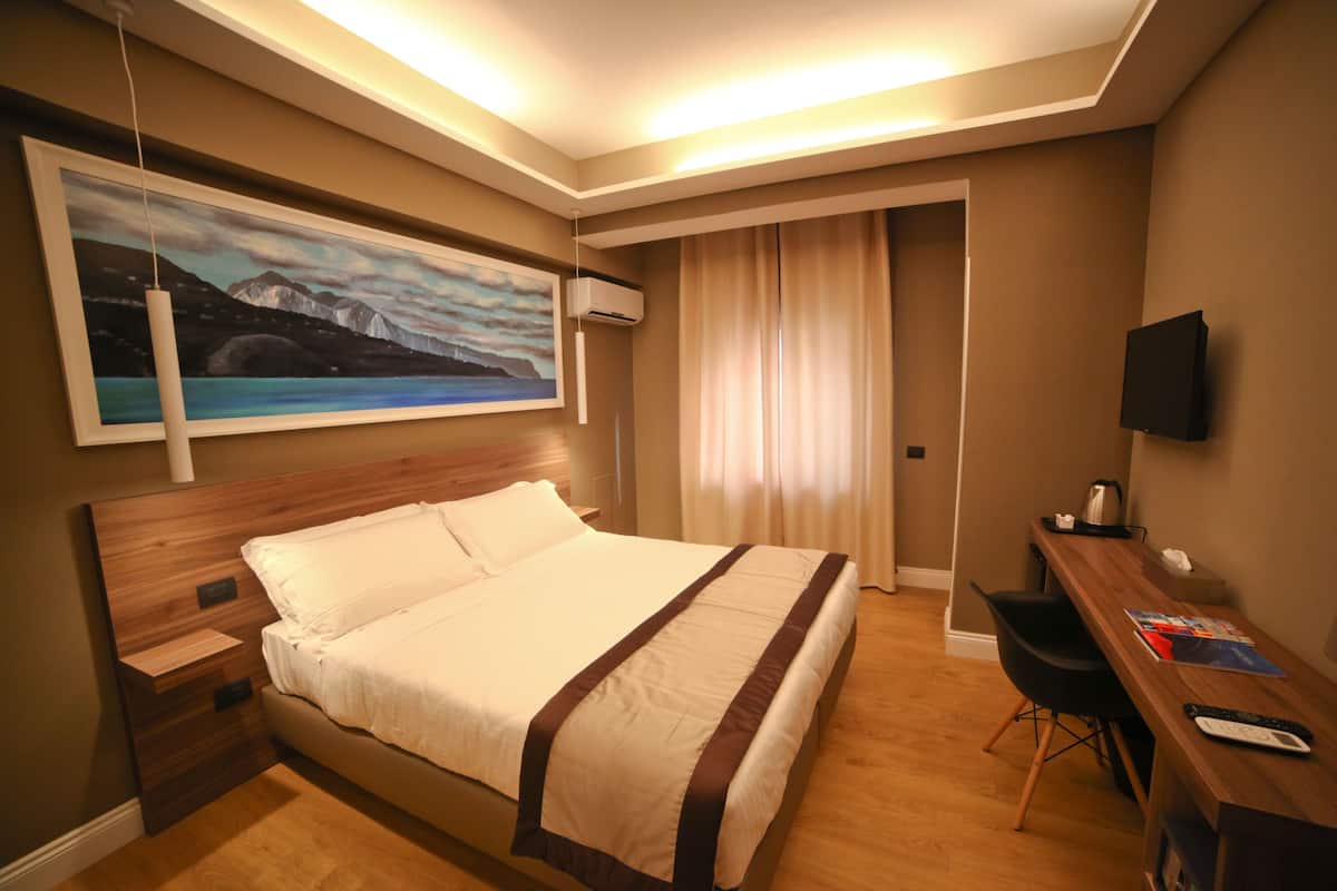 A hotel room with a large bed, a desk with a chair, a television, and a painting on the wall.