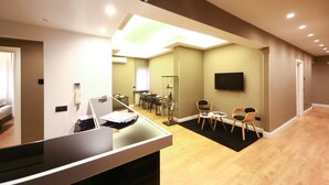 A modern hotel room with a flat-screen TV mounted on the wall, a desk with a computer, and a seating area with chairs. - 7th Floor Suite (Naples)