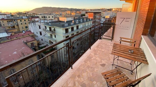 A balcony with a view of a cityscape, a 7th floor sign, and a table with benches. - 7th Floor Suite (Naples)
