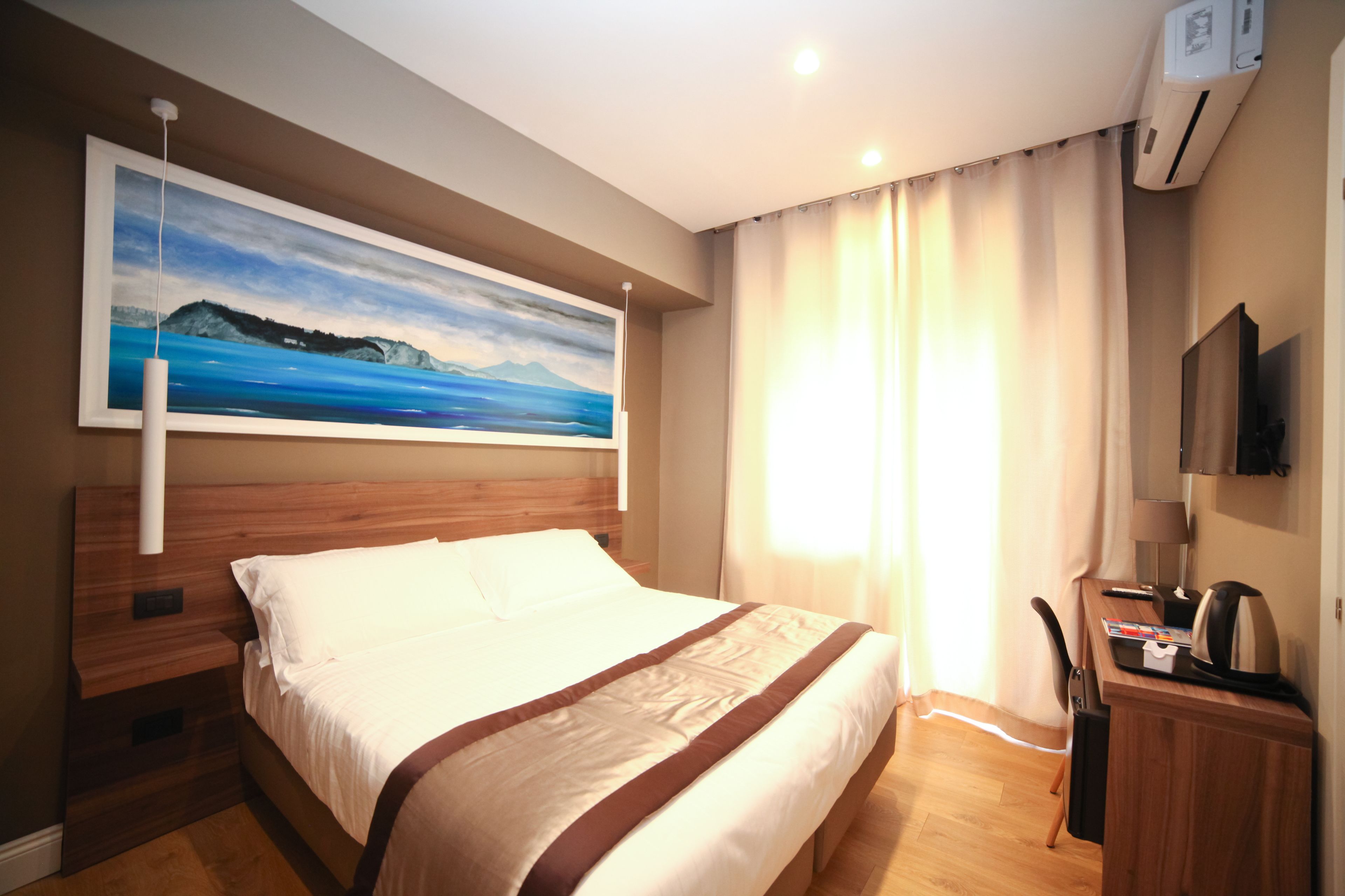 A hotel room with a bed, a desk with a chair, a television, and a painting on the wall.