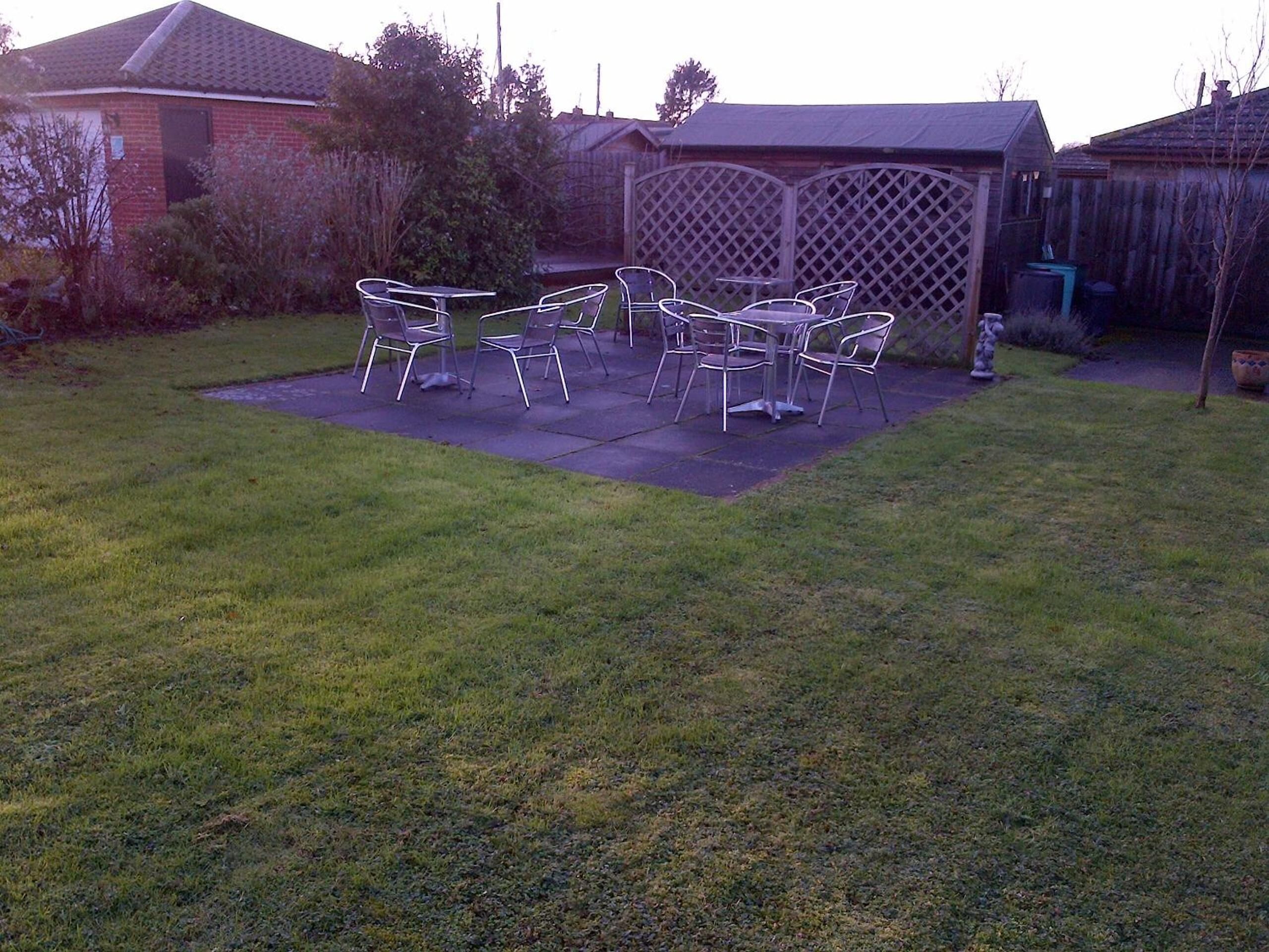 Een achtertuin met een patio tafel en stoelen, omringd door een houten schutting en een huis.