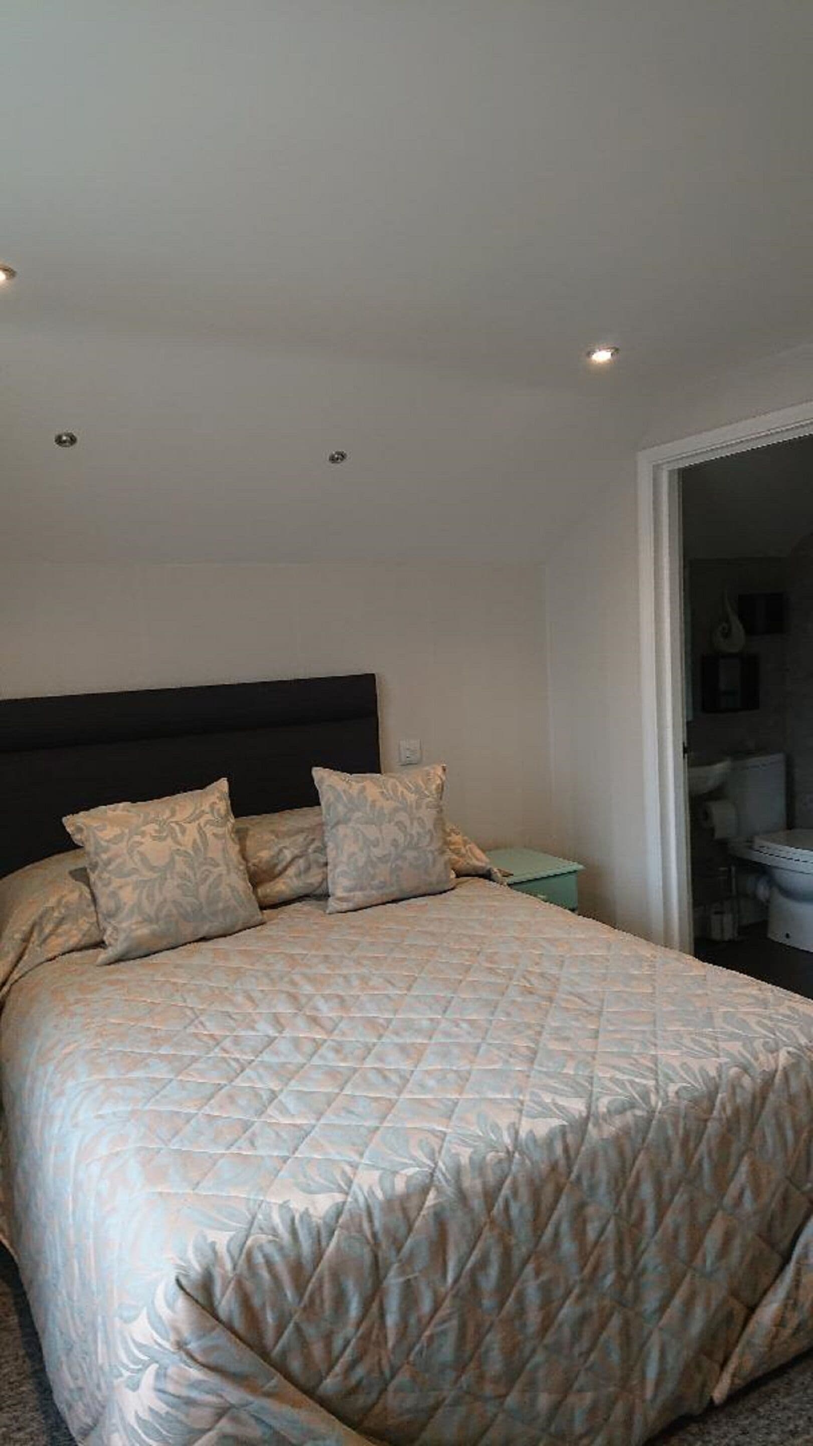 A bedroom with a large bed, a dark headboard, and a nightstand with a lamp.