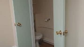 A room with a bed, a door leading to a bathroom, and a painting on the wall.