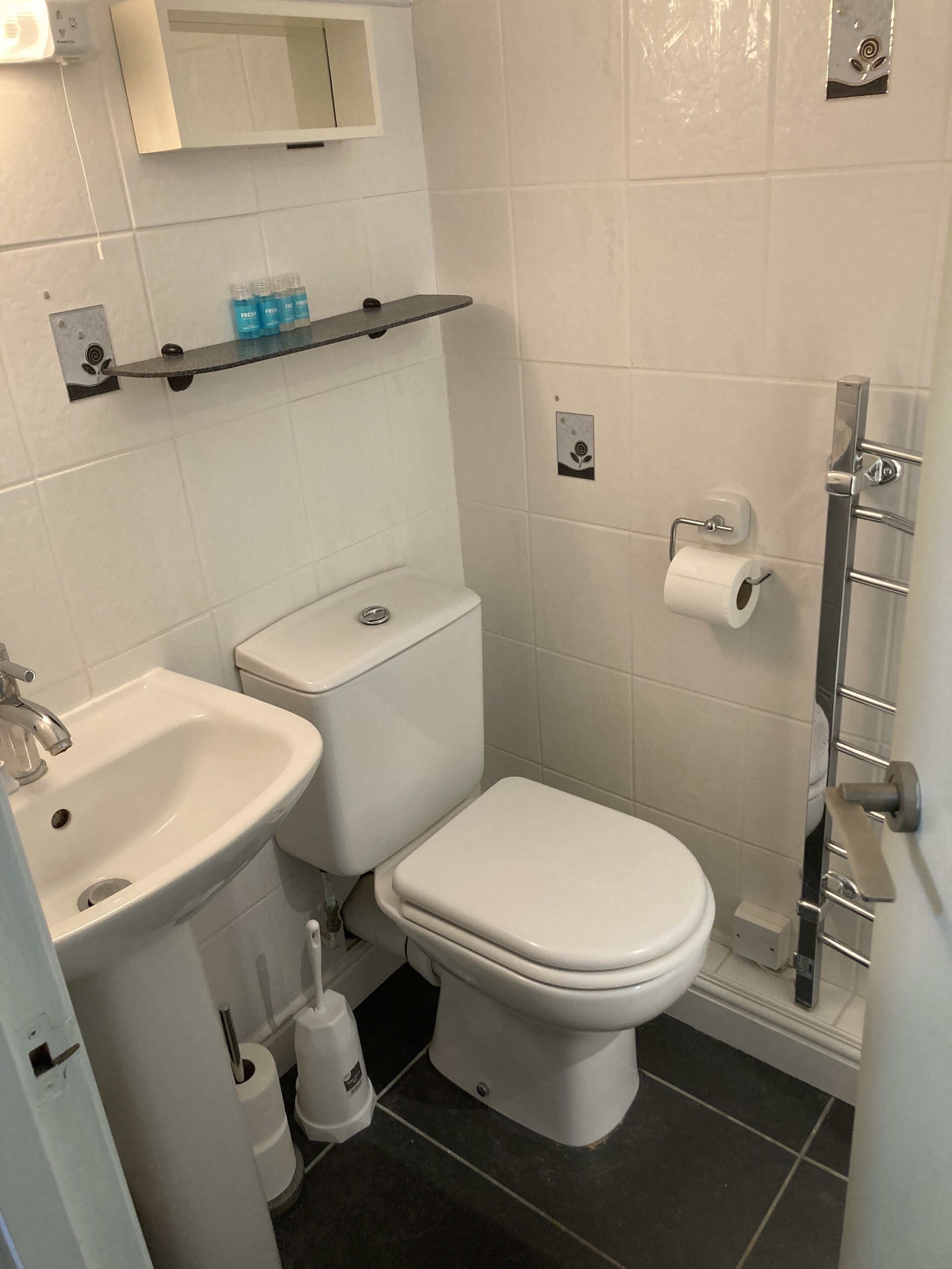 A bathroom with a white sink, toilet, and bidet. There is a shelf above the toilet holding toiletries.