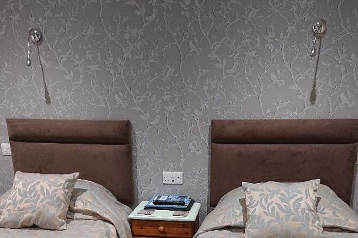 A hotel room with two beds, a nightstand, and a wall with a floral pattern.