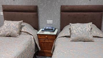 A hotel room with two beds, a nightstand, and a wall with a floral pattern.
