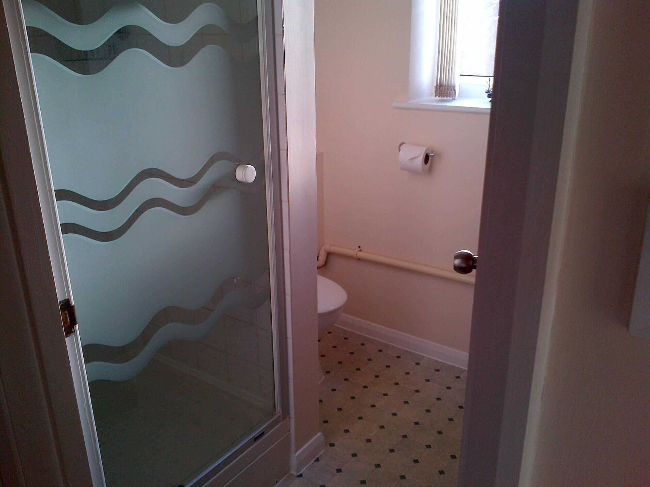 Een badkamer met een toilet, een glazen douchecabine en een vloer met een patroon.