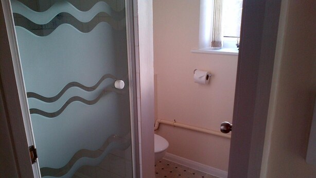 A bathroom with a toilet, a glass shower enclosure, and a patterned floor. - Grove House Hotel (Woodbridge)